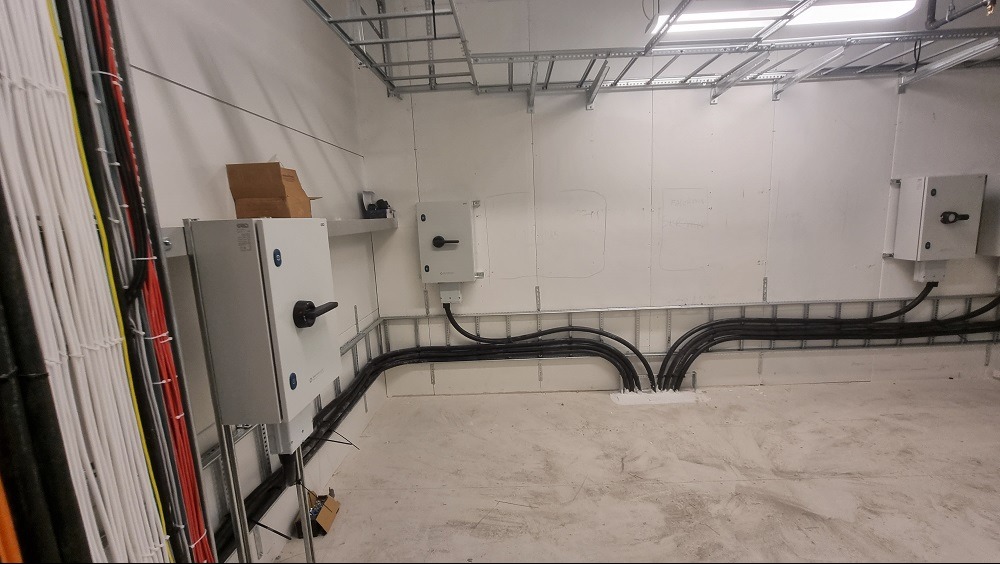 Wnętrze pomieszczenia z widocznymi szafami elektrycznymi, kablami ułożonymi w korytach oraz wiązkami przewodów po lewej stronie, ukazujące rozbudowaną infrastrukturę elektryczną.