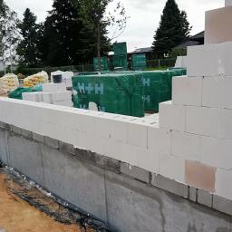 Eagle - Wznoszenie ścian z białych bloczków na fundamencie budynku w Warszawie, widoczne zapakowane materiały budowlane.