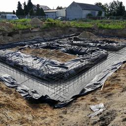 Eagle - Przygotowany zbrojony fundament pod budynek z czarną folią izolacyjną, widok z góry na wykop z piaskiem.