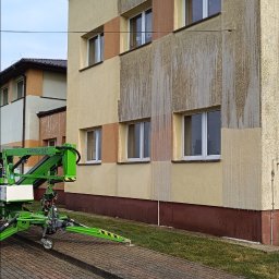Pokrycia Dachowe Paweł Poniatowski - Fragment elewacji budynku z widocznymi śladami mycia, z użyciem podnośnika koszowego i drabiny. Częściowo umyta ściana ukazuje różnicę w kolorze.