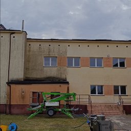 Pokrycia Dachowe Paweł Poniatowski - Częściowo umyta elewacja budynku w Łomży, widoczny podnośnik koszowy i maszyna czyszcząca. Efekt czyszczenia elewacji budynku.