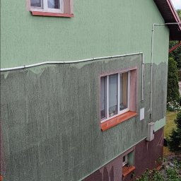 Pokrycia Dachowe Paweł Poniatowski - Fragment ściany budynku z widocznymi śladami po myciu elewacji. Górna część ściany jest czysta, dolna brudna. Widoczne okna i elementy instalacji.