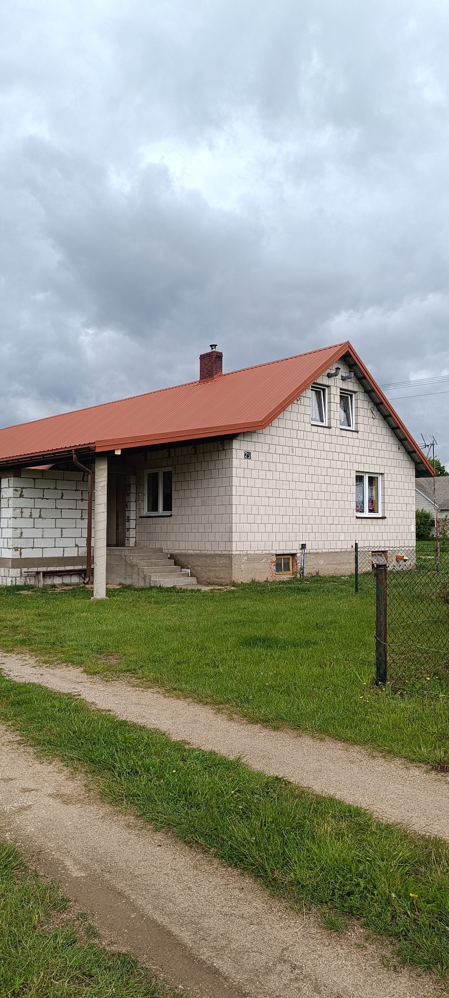Dom z białego pustaka z nowym, czerwonym dachem z blachy trapezowej. Widoczne rynny i komin. Ujęcie z poziomu gruntu, pochmurne niebo w tle.
