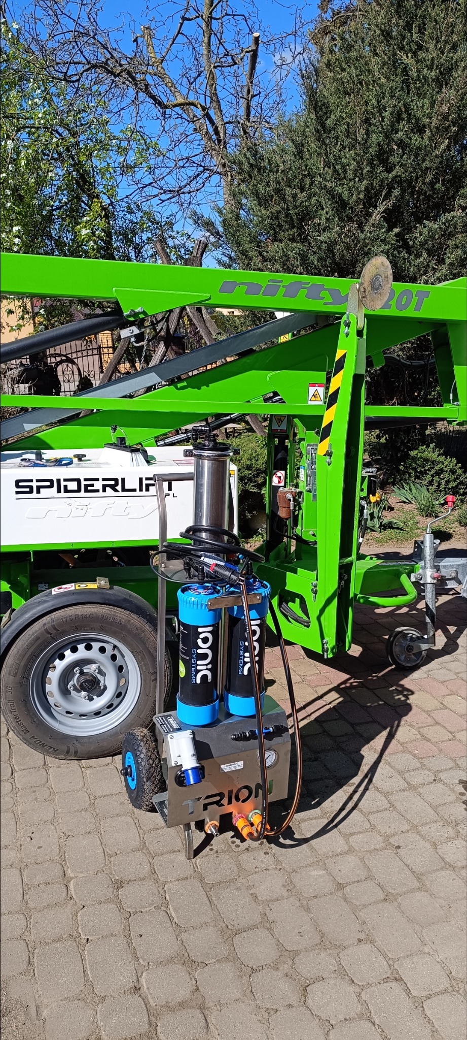 Mobilny system czyszczenia Ionic Systems Tyrion na tle podnośnika Spiderlift Nifty 20T. Urządzenie na kostce brukowej, z widocznymi filtrami i złączami.