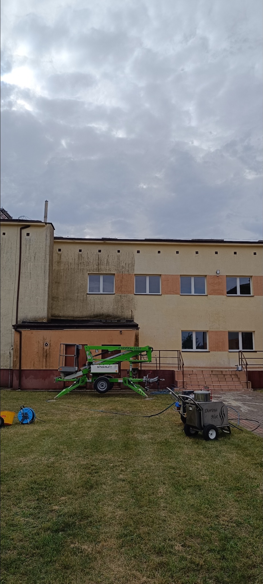 Częściowo umyta elewacja budynku w Łomży, widoczny podnośnik koszowy i maszyna czyszcząca. Efekt czyszczenia elewacji budynku.