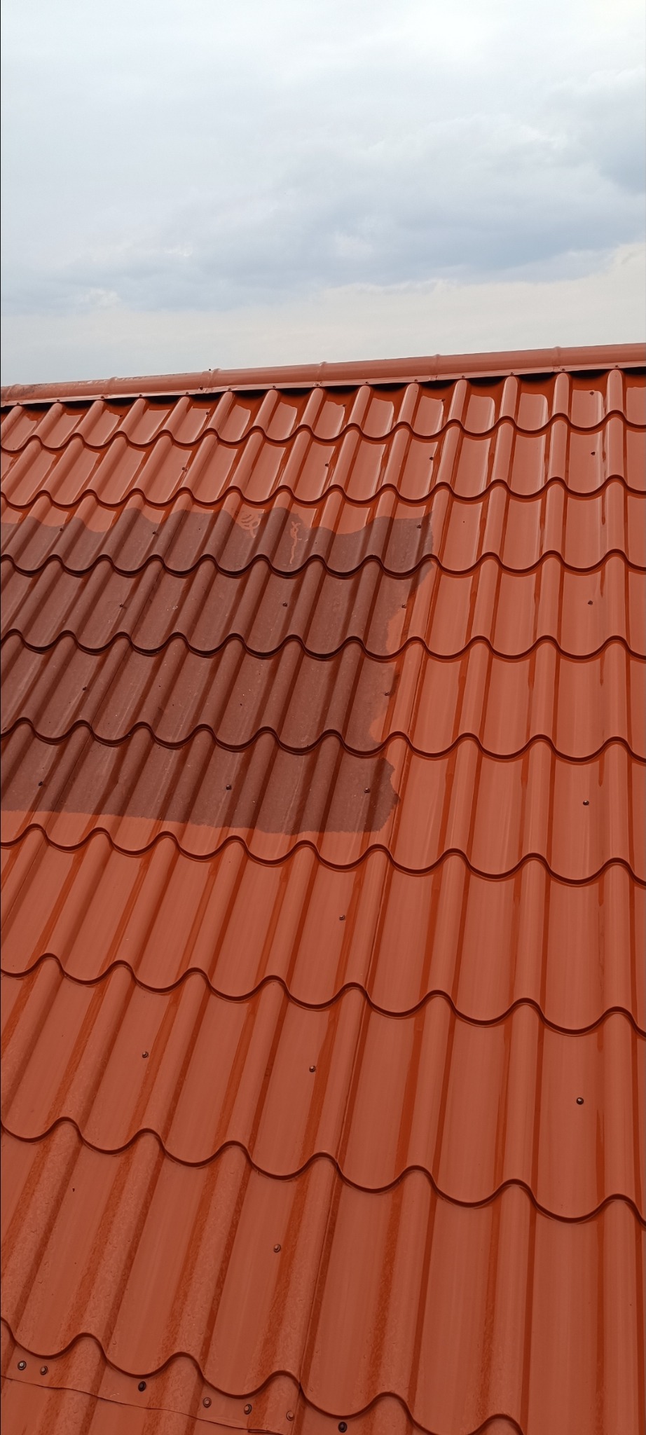 Czerwona dachówka modułowa po czyszczeniu fragmentu, widoczna różnica w kolorze. Niebo z chmurami w tle.