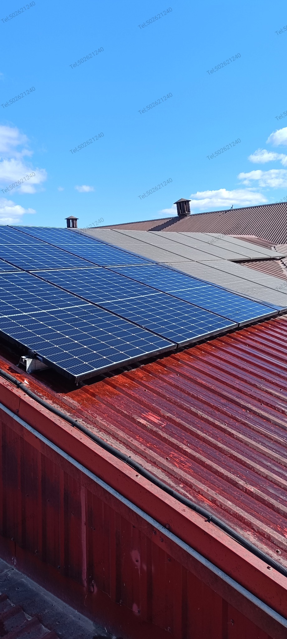 Czerwony dach z panelami słonecznymi w słoneczny dzień. Widoczne kominy i niebieskie niebo. Instalacja fotowoltaiczna na dachu z blachy trapezowej.