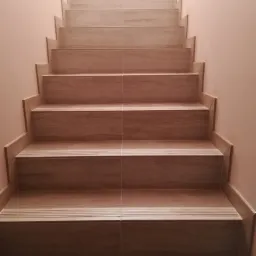 Schody wyłożone płytkami imitującymi drewno, z ryflowanymi krawędziami antypoślizgowymi, prowadzące ku górze, oświetlone od góry.