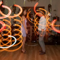 Para tańczy na parkiecie oświetlonym dynamicznymi smugami światła, z DJ-em w tle i profesjonalnym oświetleniem eventowym.