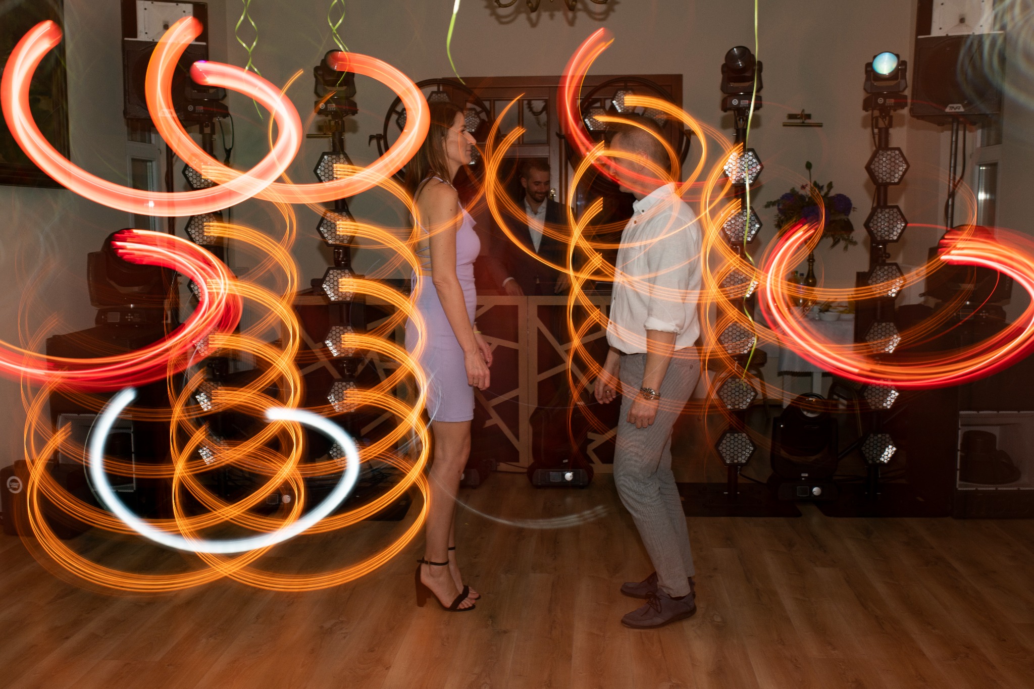 Para tańczy na parkiecie oświetlonym dynamicznymi smugami światła, z DJ-em w tle i profesjonalnym oświetleniem eventowym.