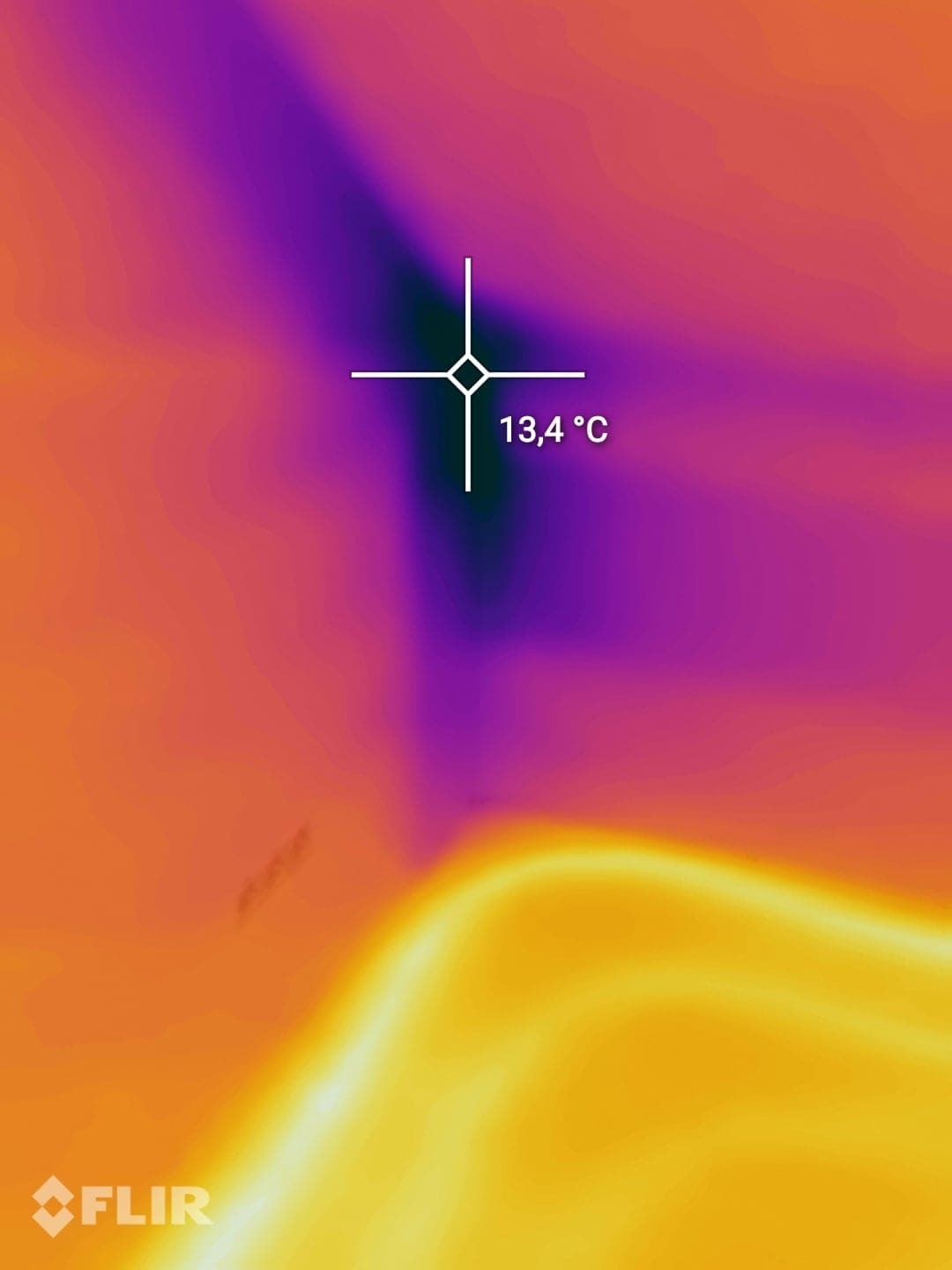Obraz termowizyjny z zaznaczonym punktem pomiaru temperatury 13,4°C, prezentujący rozkład temperatur w odcieniach pomarańczy, żółci i fioletu.