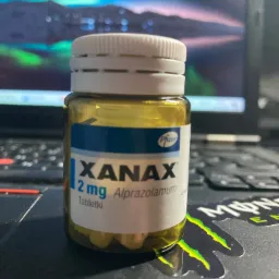Butelka tabletek Xanax 2mg firmy Pfizer na tle laptopa z wyświetlonym dynamicznym tłem.