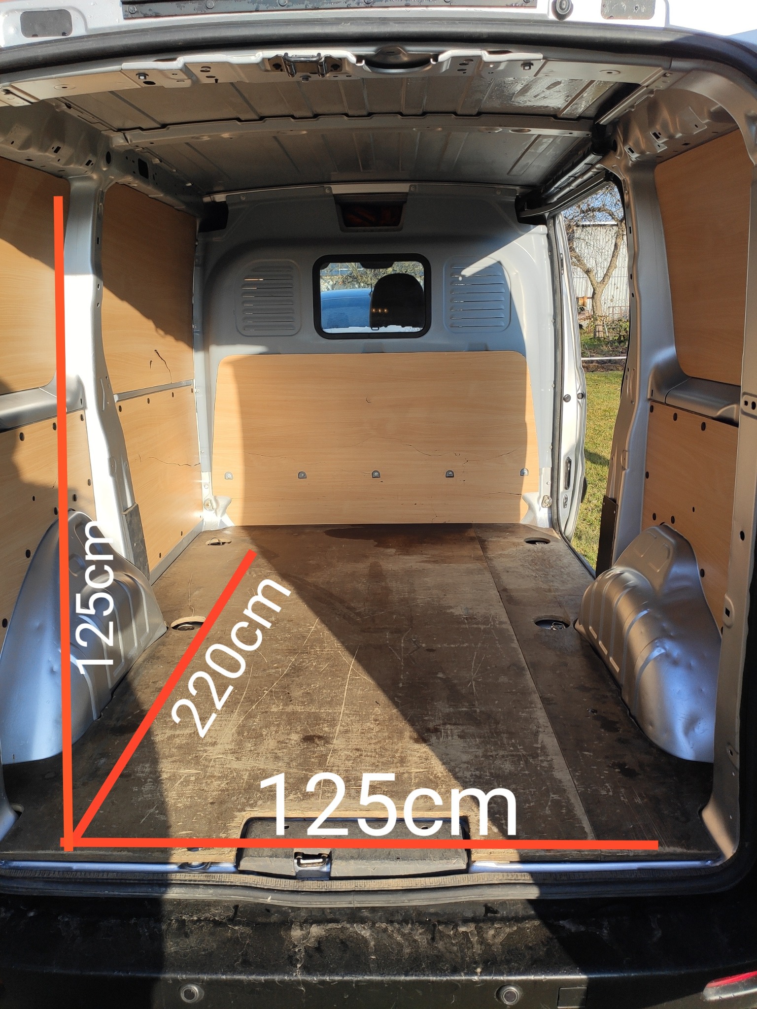 Pusta przestrzeń ładunkowa busa z deskami na ścianach i podłodze, otwarte tylne drzwi, widoczne wymiary wewnętrzne: 125cm wysokość, 220cm długość, 125cm szerokość.