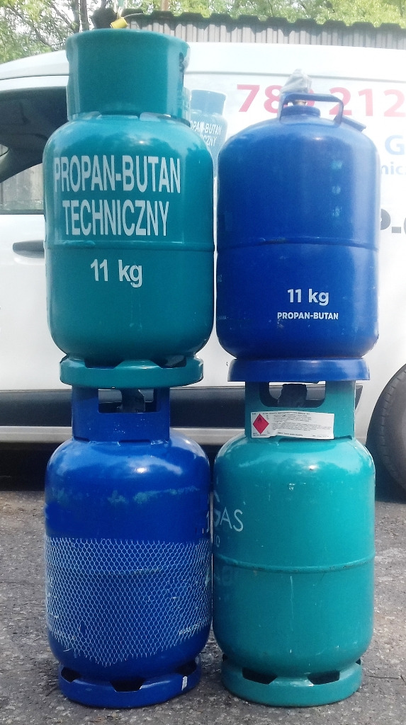 Dwa zestawy butli gazowych 11 kg, jedna niebieska z siatką ochronną, druga turkusowa z napisem 'Propan-Butan Techniczny', ustawione jedna na drugiej przed białym samochodem dostawczym.