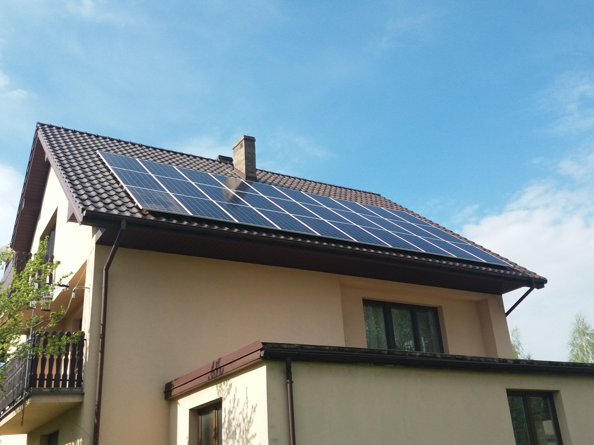 Panele słoneczne na dachu dwukondygnacyjnego domu z jasną elewacją w słoneczny dzień, widok z dołu.