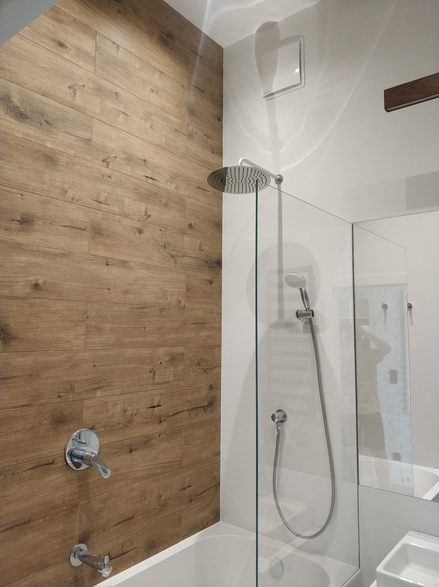 Nowoczesna łazienka z kabiną prysznicową typu walk-in, drewnopodobnymi płytkami na ścianie i chromowaną armaturą.
