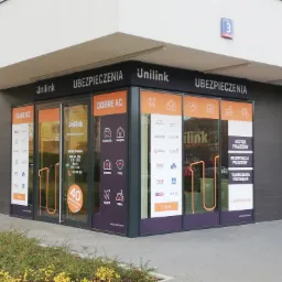 Fasada punktu stacjonarnego Unilink Ubezpieczenia z widocznymi naklejkami informacyjnymi na szybach dotyczącymi ubezpieczeń komunikacyjnych, majątkowych, na życie i zdrowotnych oraz podróżnych...