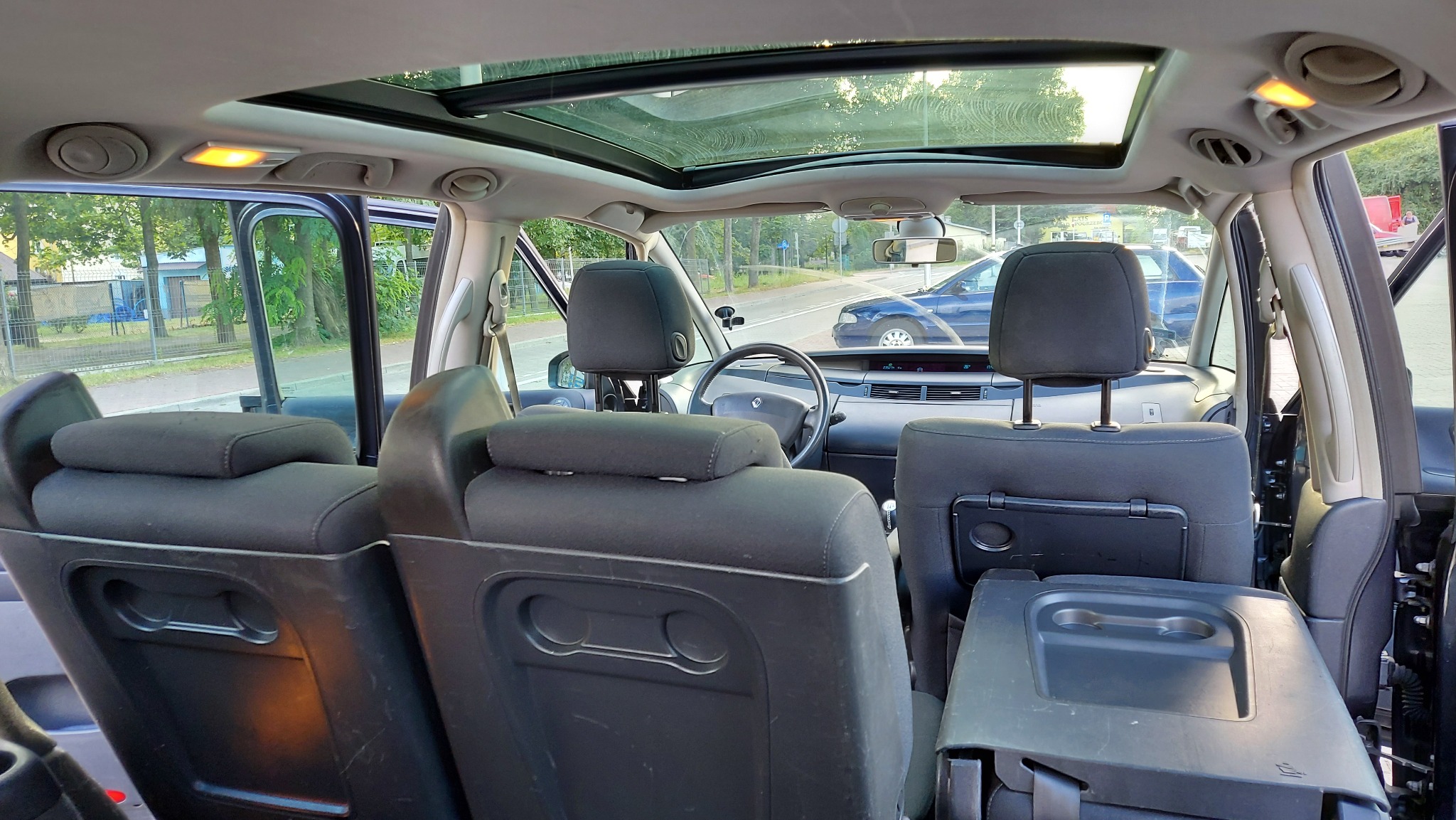 Wnętrze samochodu z widocznymi trzema rzędami siedzeń, panoramicznym dachem i widokiem na ulicę zza przedniej szyby.