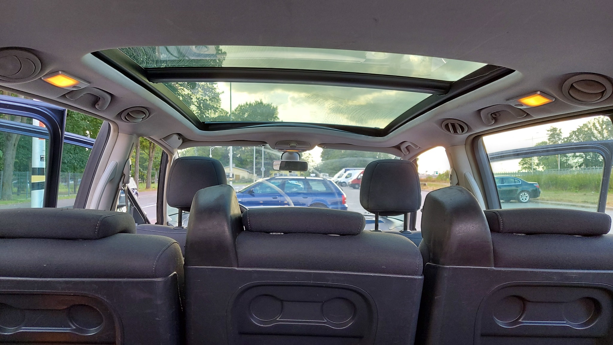 Wnętrze samochodu z widokiem na otwarty szyberdach, tylne siedzenia i widok na ulicę z zaparkowanymi pojazdami.