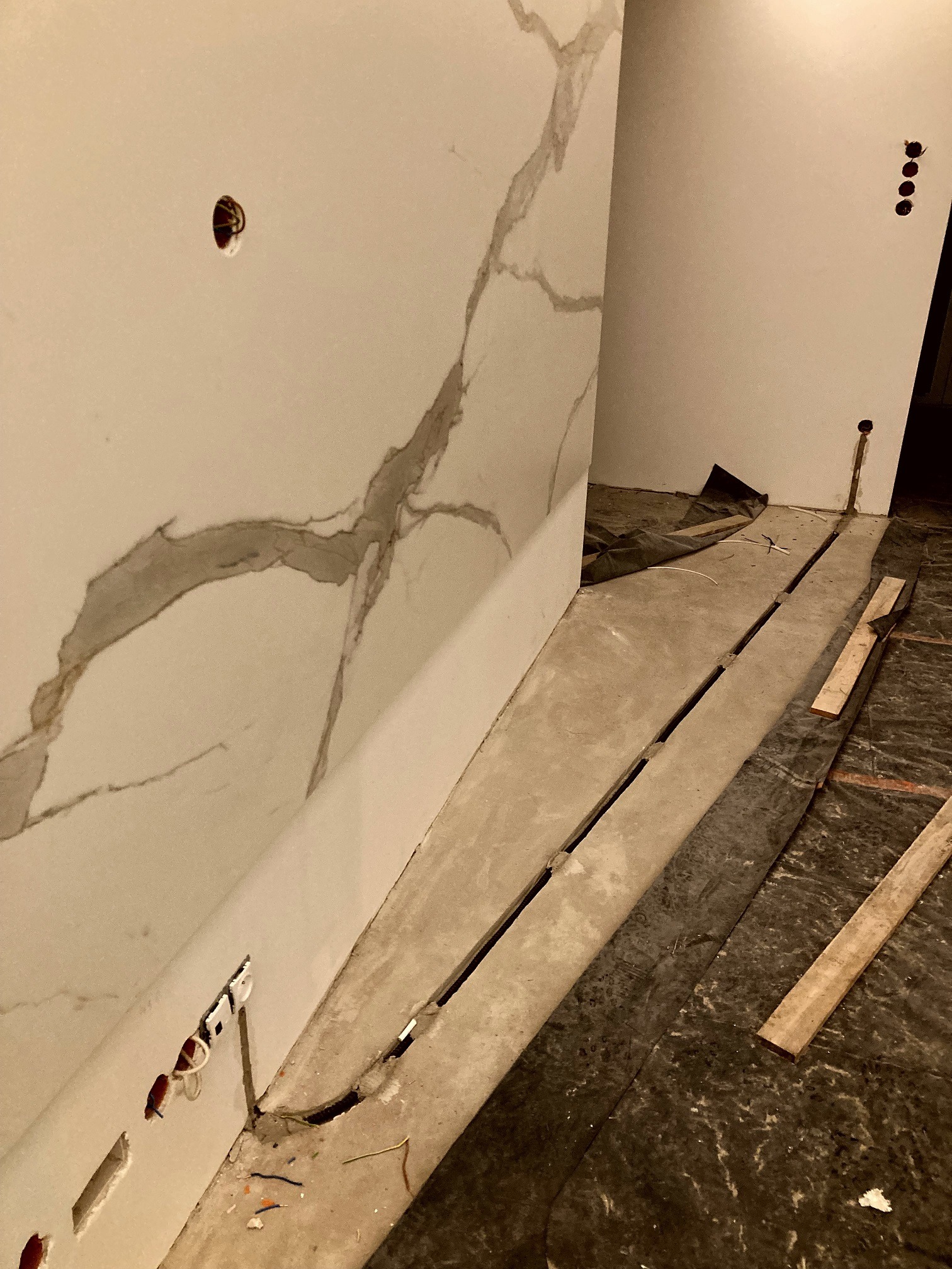 Wnętrze w trakcie prac wykończeniowych: ściana z imitacją marmuru z przygotowanymi otworami na gniazdka elektryczne i przewody, widoczne kable, fragment podłogi zabezpieczony folią malarską.