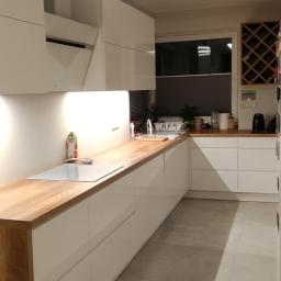 Ardbed Invest - Nowoczesna kuchnia z białymi szafkami i drewnianym blatem, oświetlona punktowymi lampami sufitowymi, z widocznym okapem i półką na wino.