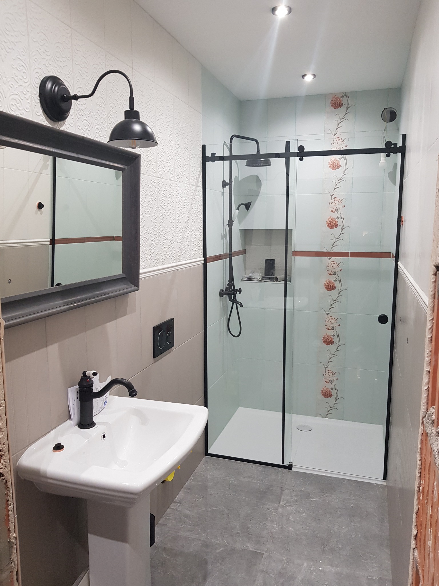 Nowoczesna łazienka z kabiną prysznicową typu walk-in z czarnymi profilami, umywalką na postumencie z czarną armaturą i oświetleniem w stylu retro.