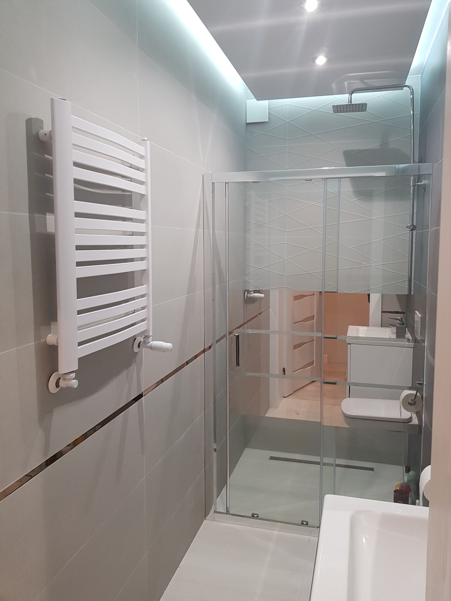 Nowoczesna łazienka w Płochocinie z przeszkloną kabiną prysznicową, grzejnikiem drabinkowym i subtelnym oświetleniem LED.
