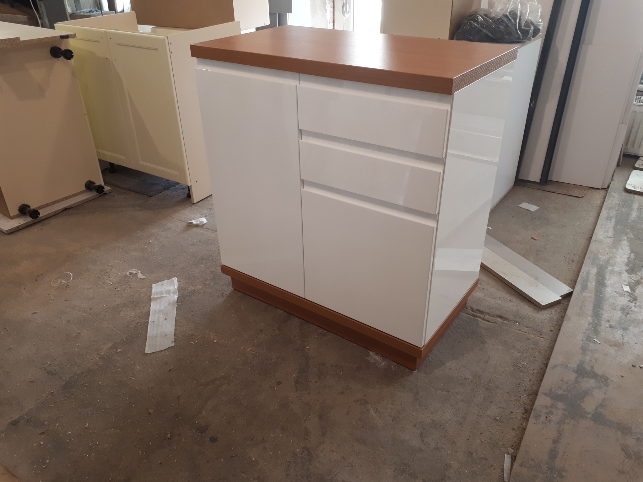 Biała szafka z trzema szufladami i drewnianym blatem na tle podłogi w trakcie montażu mebli.