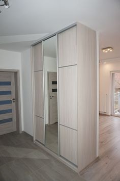 Jasna szafa przesuwna z lustrem w przedpokoju, widoczne drzwi z niebieskimi akcentami i podłoga z paneli.