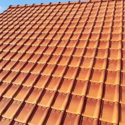 Pomarańczowa dachówka ceramiczna ułożona na dachu domu, widok z dołu pod ostrym kątem w słoneczny dzień.