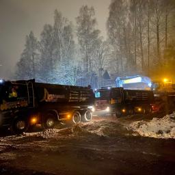 Wyburzenia Śląsk - Dwa czarne samochody ciężarowe z logo firmy 'Wyburzenia Śląsk' stoją na błotnistym terenie w nocy, w tle widać koparkę i ośnieżone drzewa.