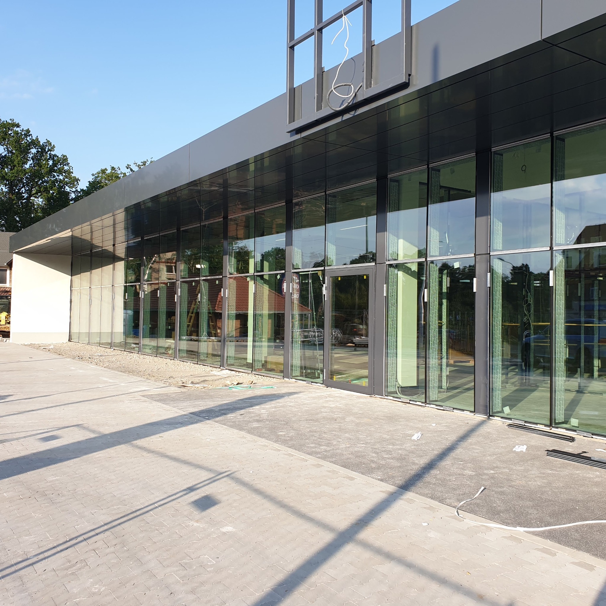 Nowoczesny budynek z aluminiowymi oknami i szklanymi drzwiami w trakcie montażu, widoczne elementy konstrukcyjne i przewody na dachu.