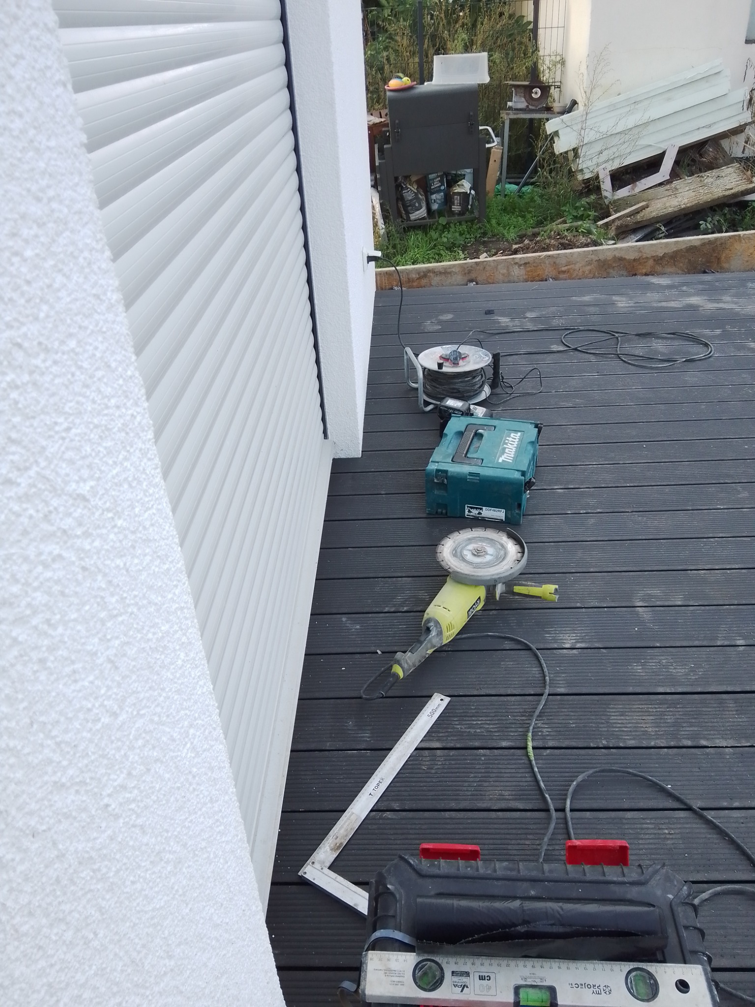 Elewacja z zamontowaną roletą zewnętrzną, na podeście z desek kompozytowych leżą narzędzia: szlifierka kątowa, poziomica, kątownik, przedłużacz, skrzynka narzędziowa.