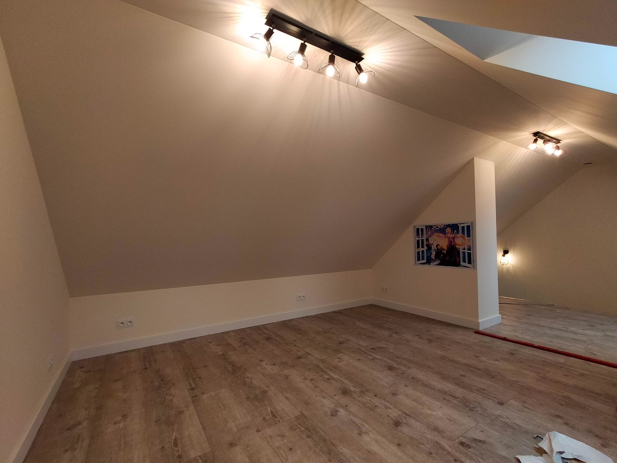 Poddasze po remoncie z panelami podłogowymi, oświetleniem punktowym i obrazkiem na ścianie