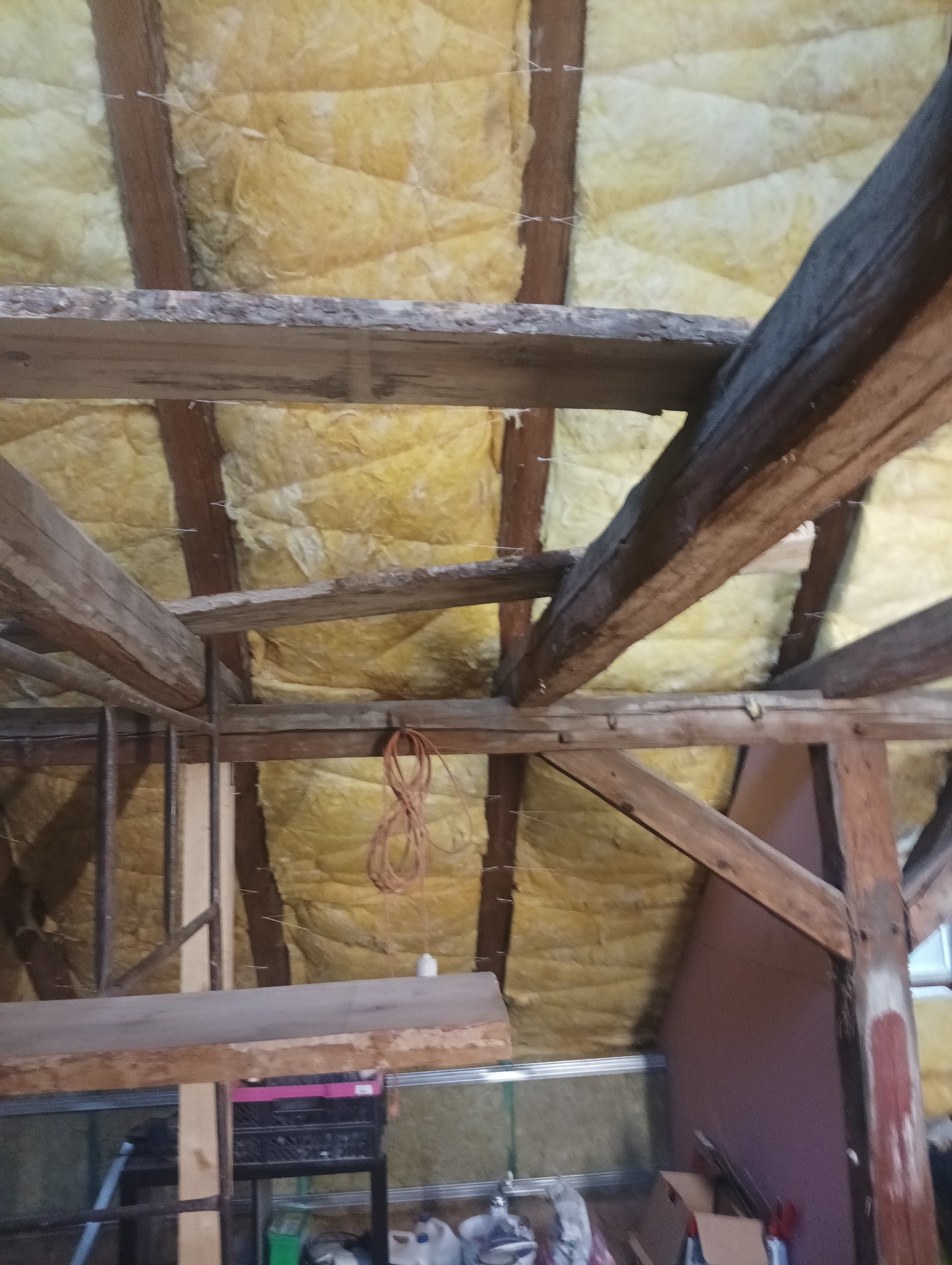 Izolacja poddasza wełną mineralną, widoczne drewniane krokwie i przewody elektryczne.