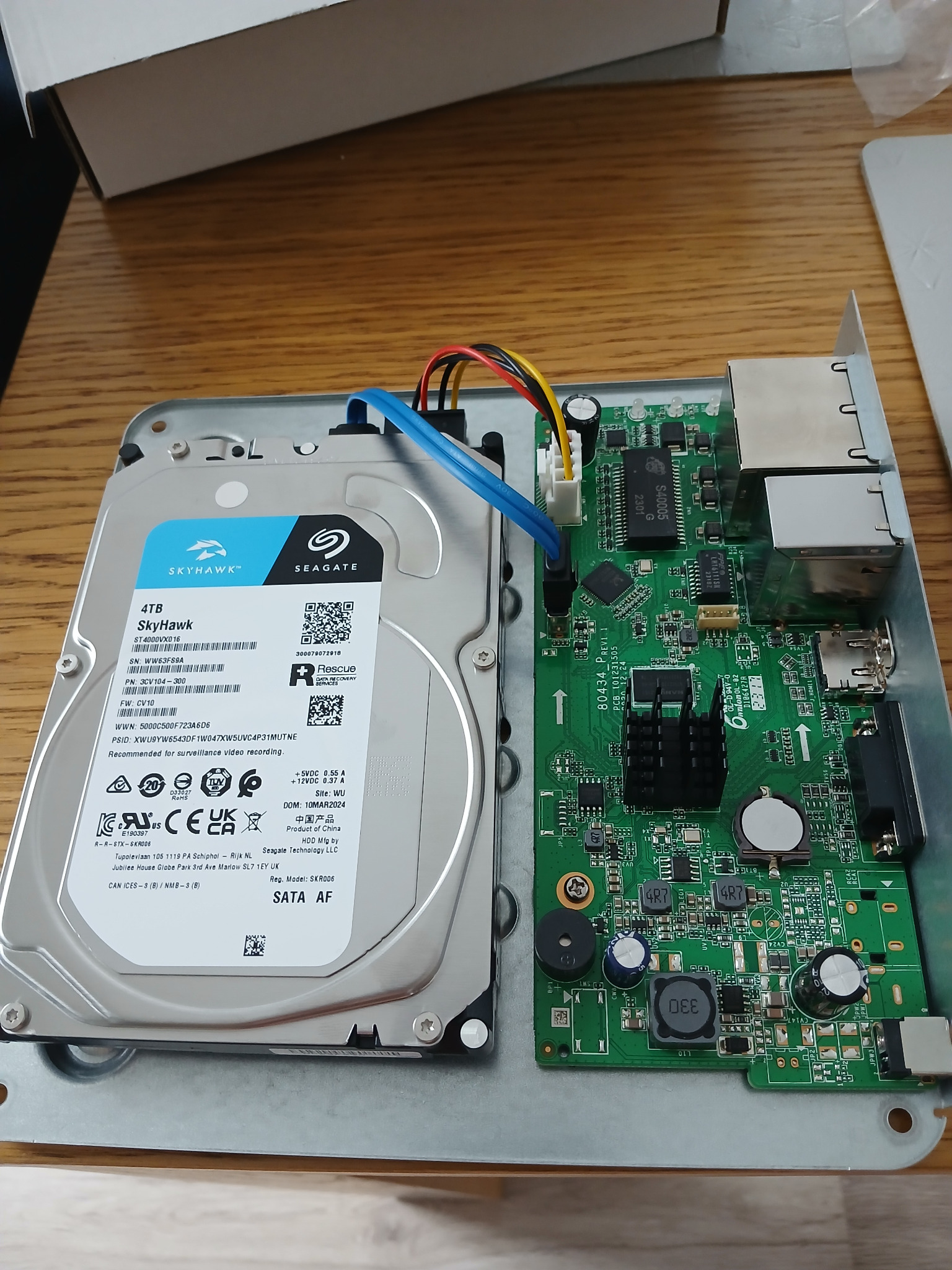 Wnętrze rejestratora monitoringu z zamontowanym dyskiem twardym Seagate SkyHawk 4TB, widoczne okablowanie i płyta główna z elementami elektronicznymi.