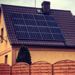 Fox soluction - Dom jednorodzinny z brązowym dachem, na którym zamontowano panel słoneczny. W tle widoczny ceglany komin i pochmurne niebo. Na pierwszym planie drewniany płot.