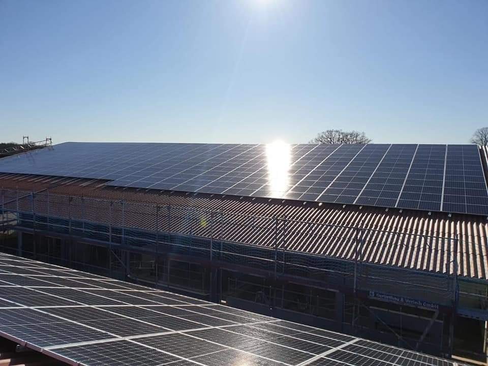 Panele słoneczne na dachu budynku przemysłowego, widoczne rusztowania i refleksy słoneczne.