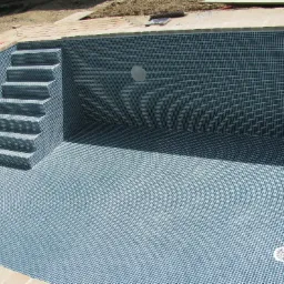 Pusty basen wyłożony niebieską mozaiką z widocznymi schodami wejściowymi i elementami instalacji w ścianach.