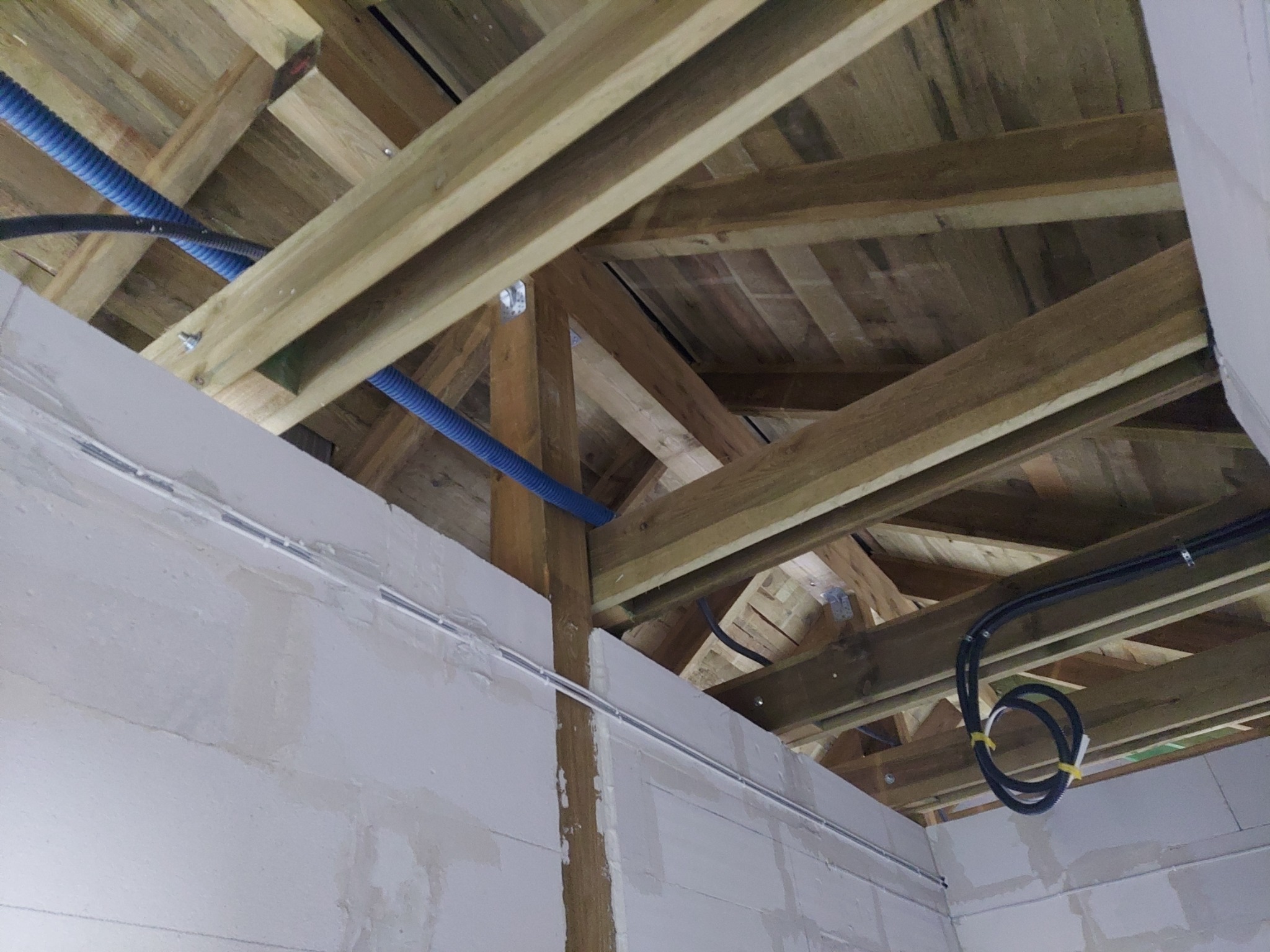 Niebieskie i czarne rury instalacyjne prowadzone wzdłuż drewnianej konstrukcji dachu i sufitu w trakcie prac wykończeniowych.