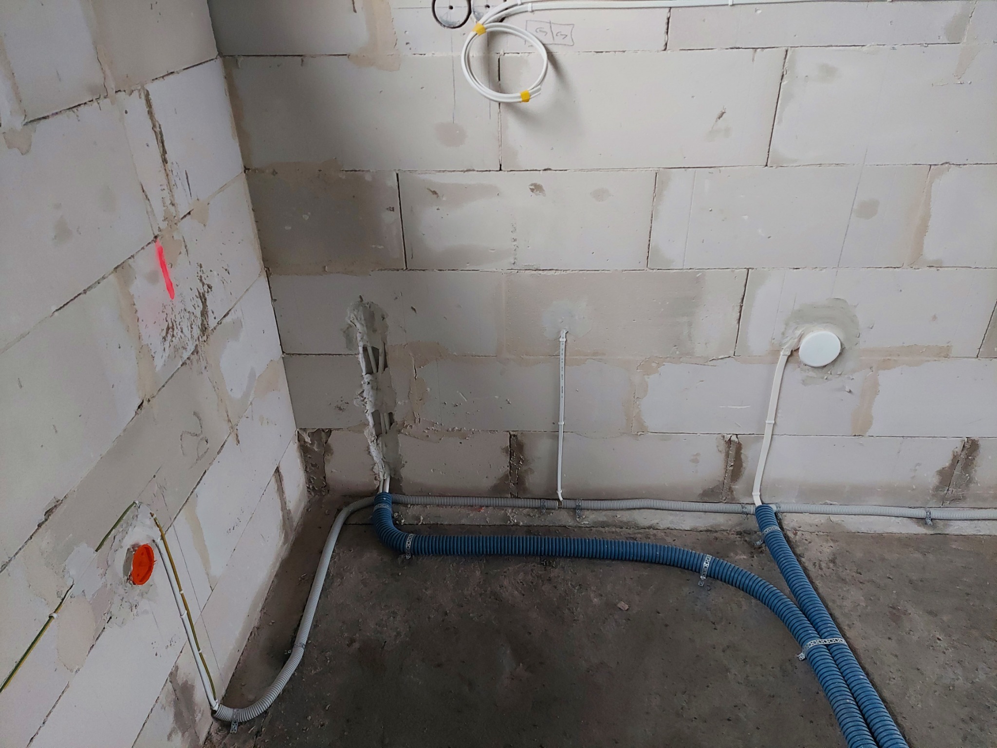 Wnętrze w trakcie prac elektrycznych: widoczne kable w peszlach na podłodze i wyprowadzenia w ścianach z betonu komórkowego, z zaznaczoną pionową linią czerwoną farbą.