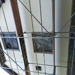 Elewacja domu w Piastowie w trakcie prac, widok z rusztowania, okna zabezpieczone folią, świeżo nałożony jasny tynk.