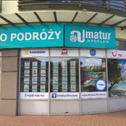 Fasada budynku z szyldem 'BIURO PODRÓŻY Almatur Wrocław', plakaty ofert wakacyjnych w oknach, logotypy Rainbow, Itaka, TUI i Coral Travel.