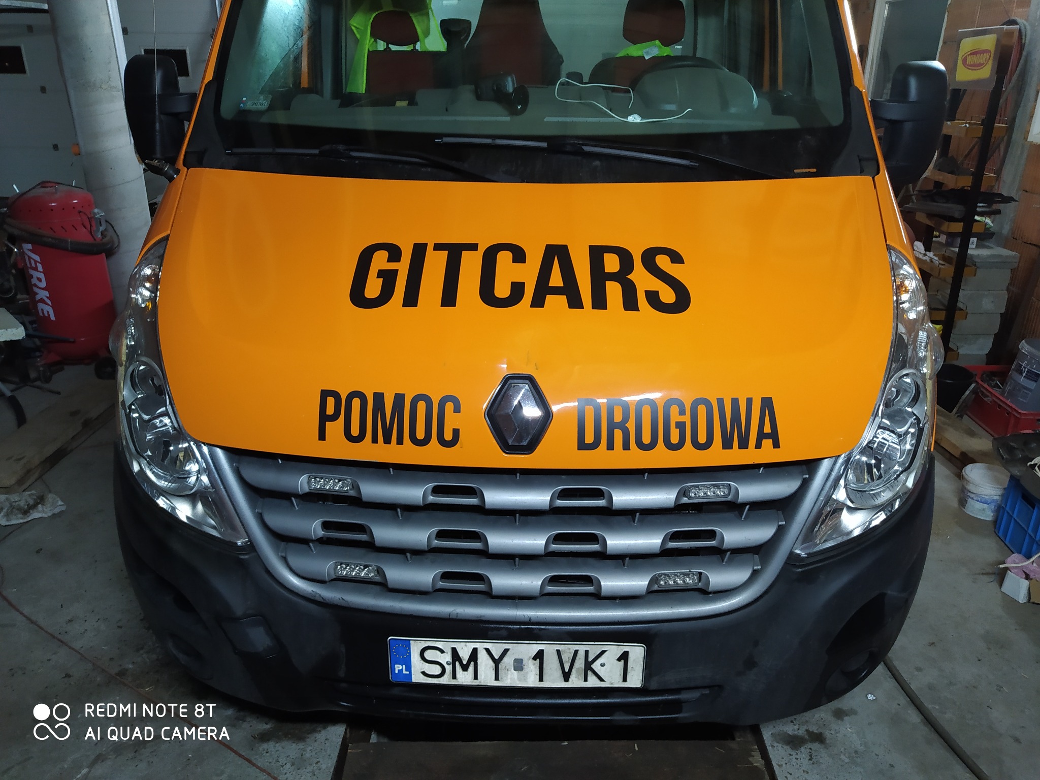 Pomarańczowy samochód pomocy drogowej firmy GITCARS z Przyrowa, z widocznym numerem rejestracyjnym SMY 1VK1, zaparkowany w garażu.