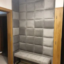 Szara, tapicerowana ściana z siedziskiem w korytarzu, obok drewnianych drzwi.