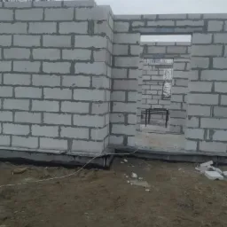 Wznoszenie ścian parteru z betonu komórkowego, widoczne spoiny i fundament izolowany czarną folią, surowy stan budowy.