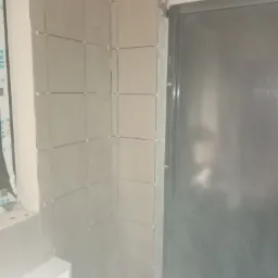 Świeżo ułożone, jasnoszare płytki ścienne z krzyżykami dystansowymi, widoczne przy ościeżnicy drzwi, w trakcie prac wykończeniowych.