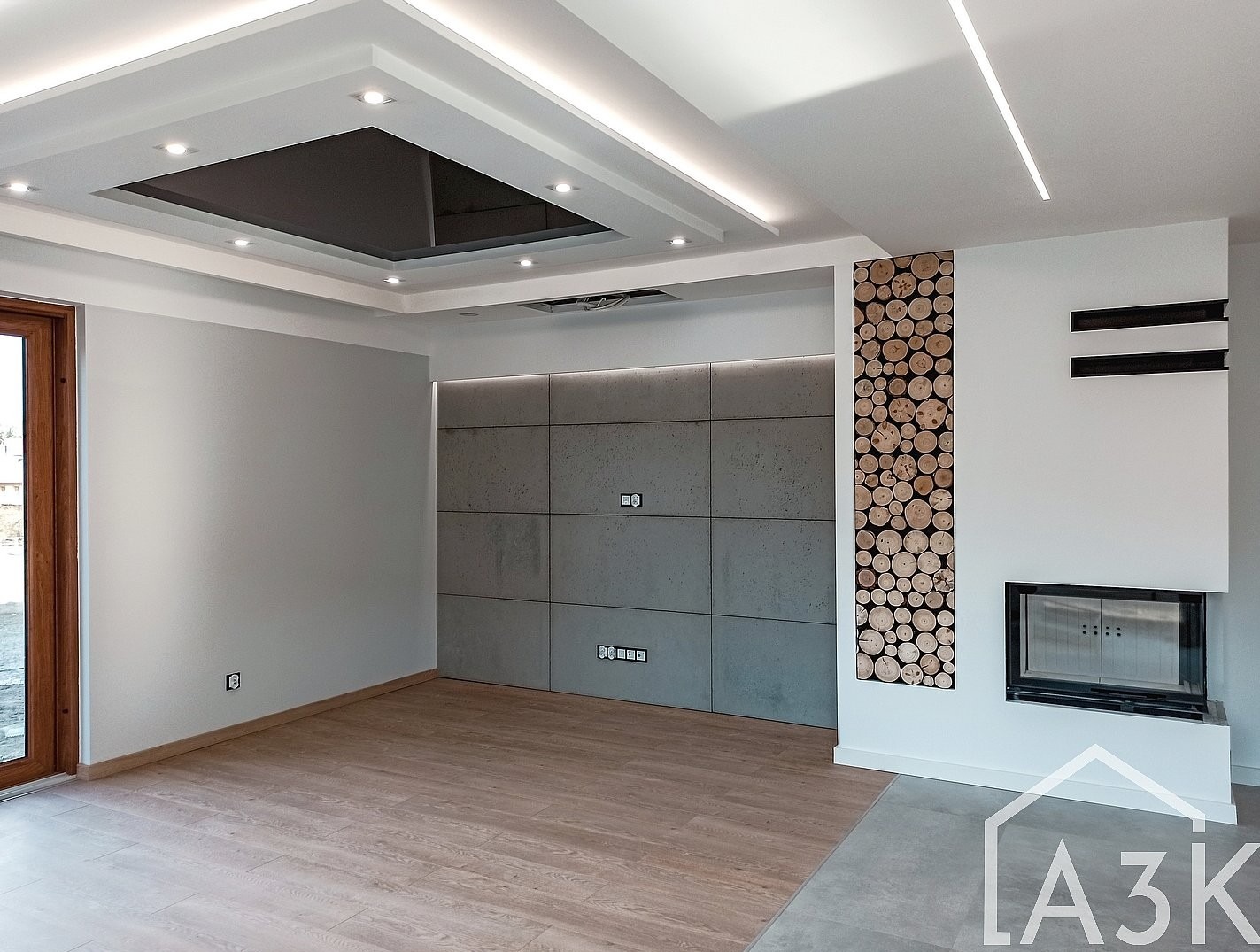 Nowoczesny salon z klimatycznym kominkiem w otoczce płyt betonowych podkreślonych sufitem napinanym.