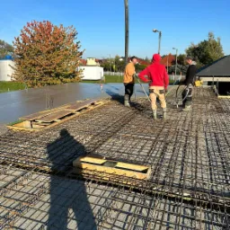Prace betoniarskie w Płońsku: trzech pracownik&oacute;w na zbrojeniu, w tle wylany beton i pompa do betonu.