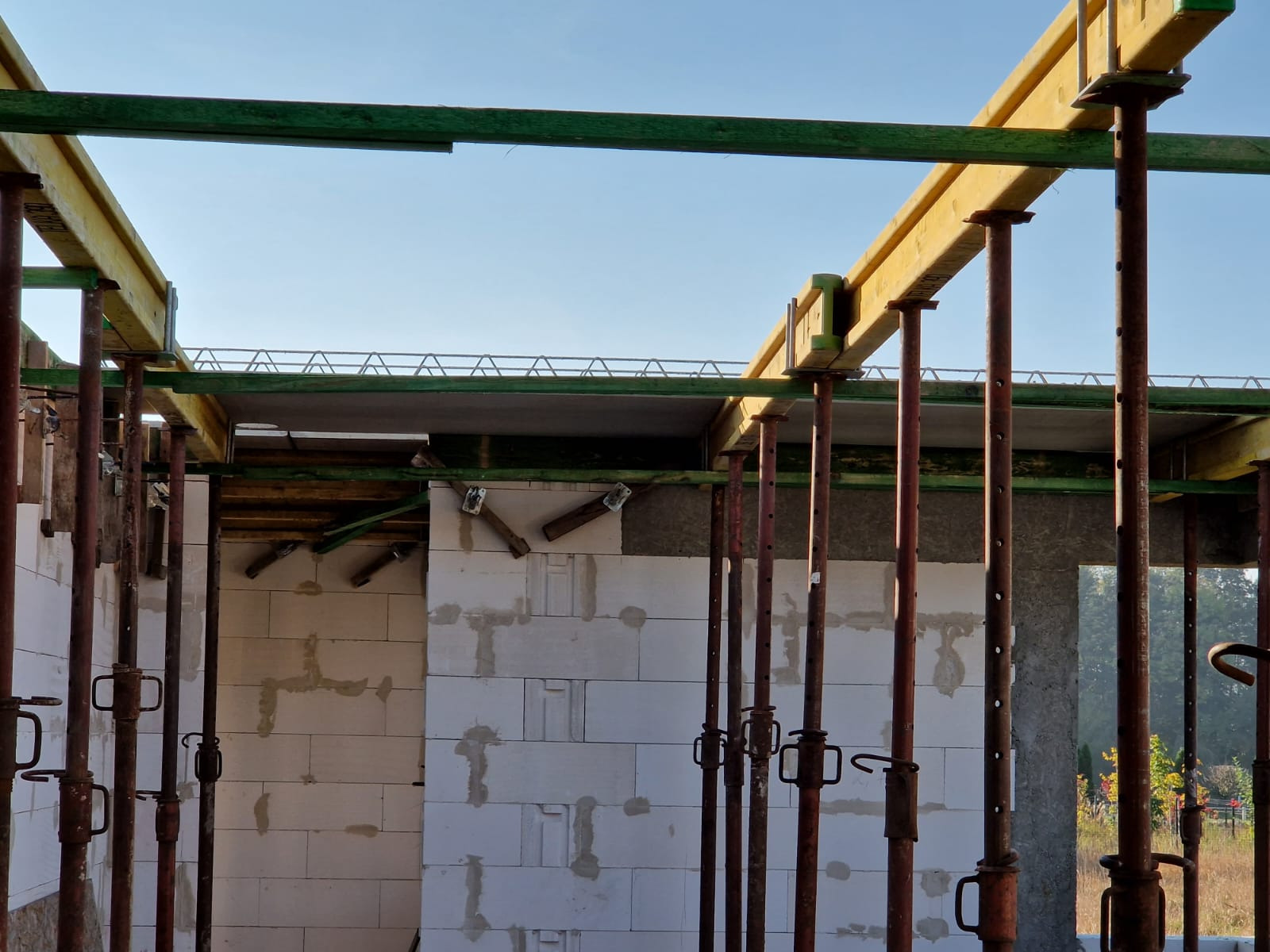 Konstrukcja szalunkowa stropu wsparta na stalowych stemplach, widoczne bloczki z betonu komórkowego tworzące ściany budynku w trakcie budowy, jasne niebo w tle.